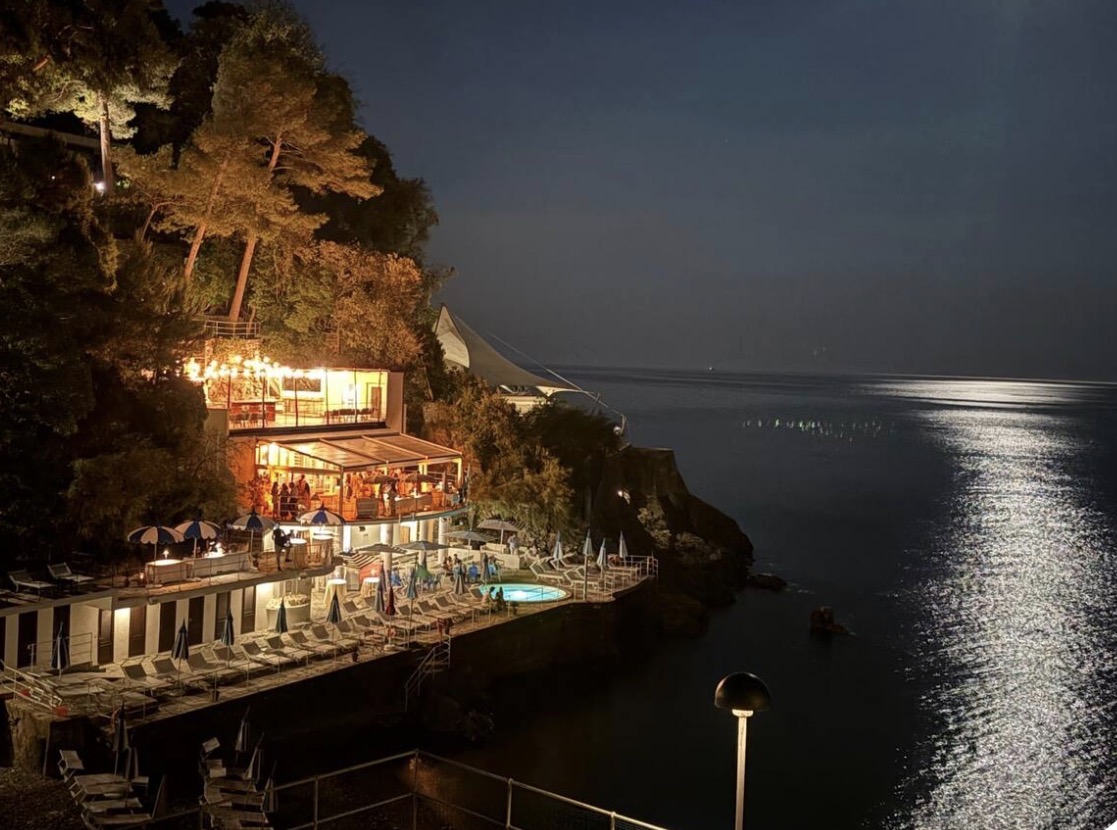 Seaside beach club lit up at night along the Ligurian coast
